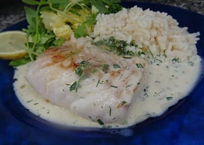 Cabillaud sauce Normande avec riz et salade dans une assiette bleue du restaurant "Les Délices du Cotentin à Sainte mère église.